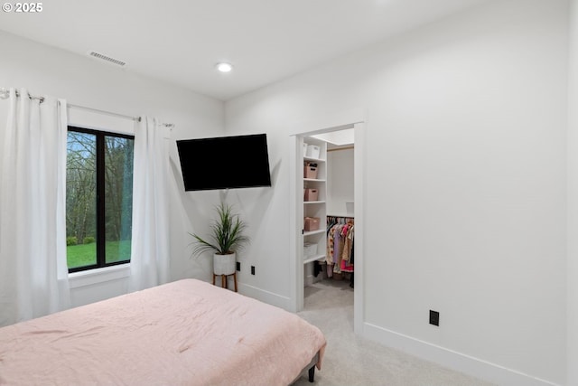 bedroom featuring a walk in closet, baseboards, light colored carpet, and multiple windows