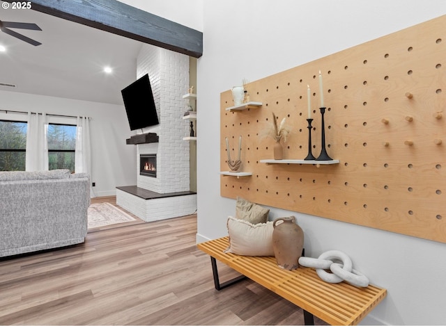 living area with wood finished floors, visible vents, beam ceiling, ceiling fan, and a brick fireplace