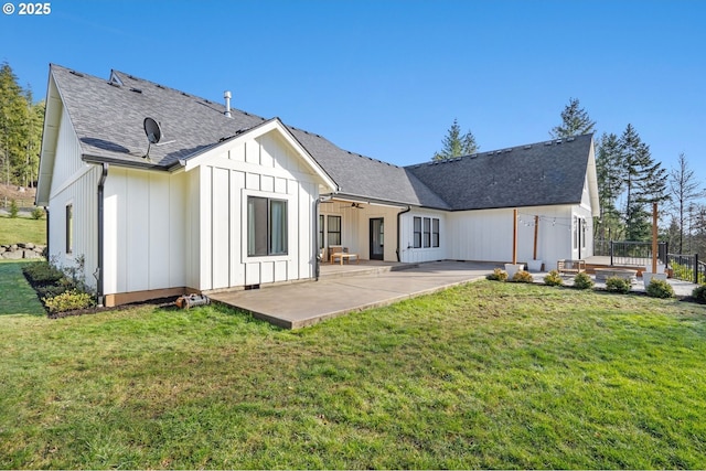 rear view of property featuring board and batten siding, a shingled roof, a wooden deck, a lawn, and a patio area