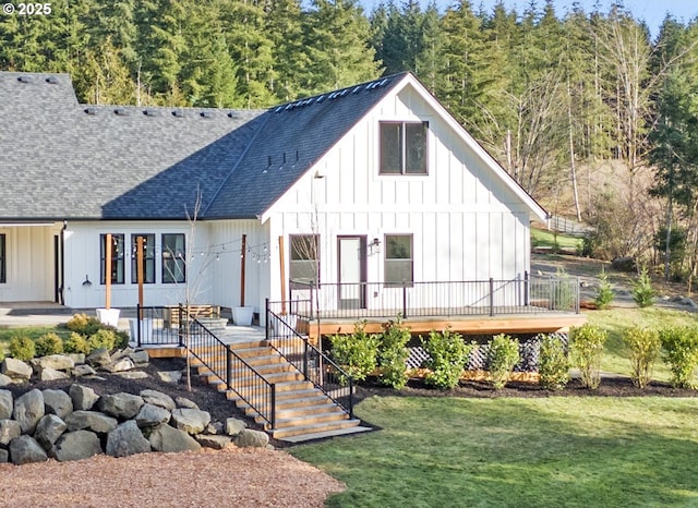 back of house featuring a lawn, a deck, board and batten siding, a shingled roof, and stairs