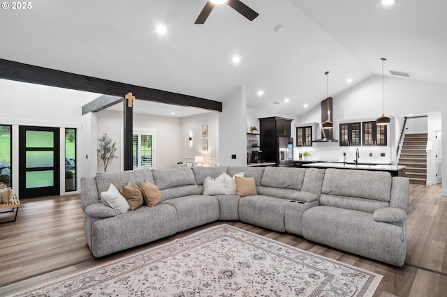 living area featuring visible vents, ceiling fan, stairway, light wood-type flooring, and high vaulted ceiling