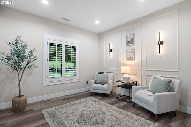 living area featuring visible vents, wood finished floors, recessed lighting, a decorative wall, and baseboards