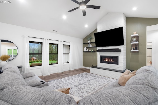 living room featuring wood finished floors, baseboards, visible vents, lofted ceiling, and a large fireplace