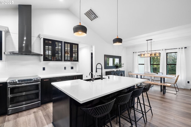 kitchen with dark cabinetry, double oven range, visible vents, light countertops, and wall chimney exhaust hood