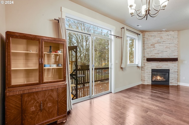 entryway with a chandelier, wood-type flooring, and a stone fireplace