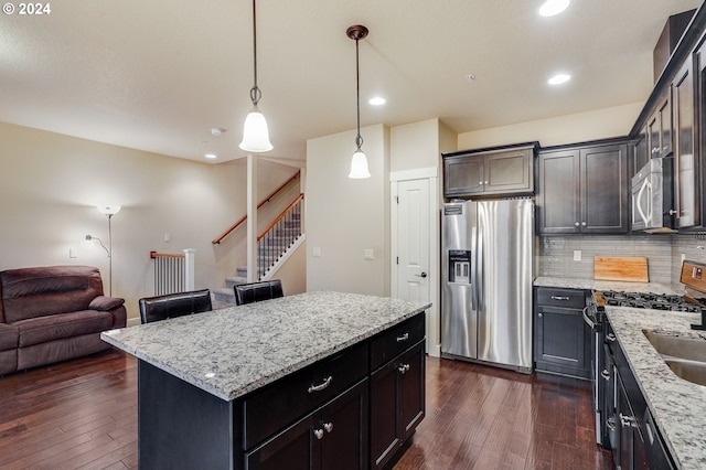 kitchen with backsplash, light stone counters, stainless steel appliances, pendant lighting, and a center island