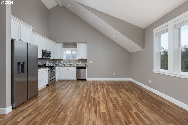 kitchen featuring high vaulted ceiling, stainless steel appliances, white cabinets, and hardwood / wood-style flooring