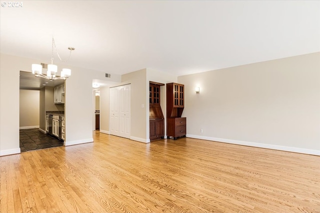 unfurnished living room featuring an inviting chandelier and light hardwood / wood-style flooring