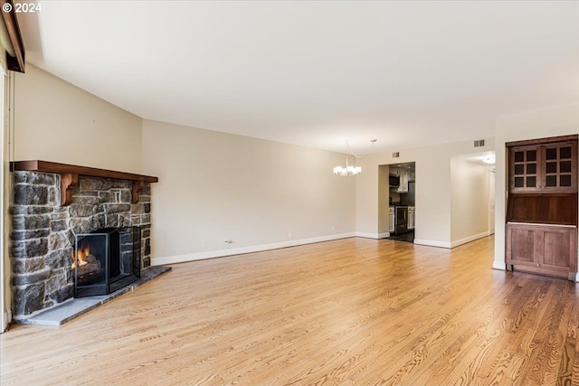 unfurnished living room featuring a stone fireplace, light wood-type flooring, and a notable chandelier