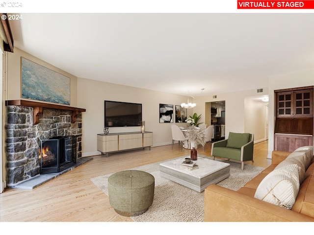 living room with a stone fireplace, wood-type flooring, and a notable chandelier