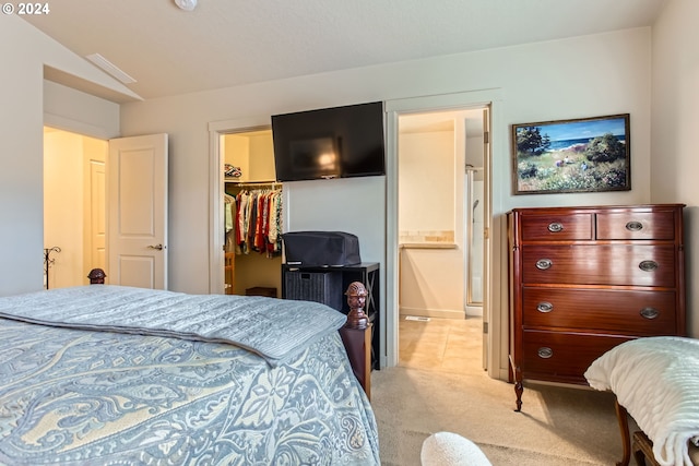 bedroom with a closet, light colored carpet, a spacious closet, and ensuite bath