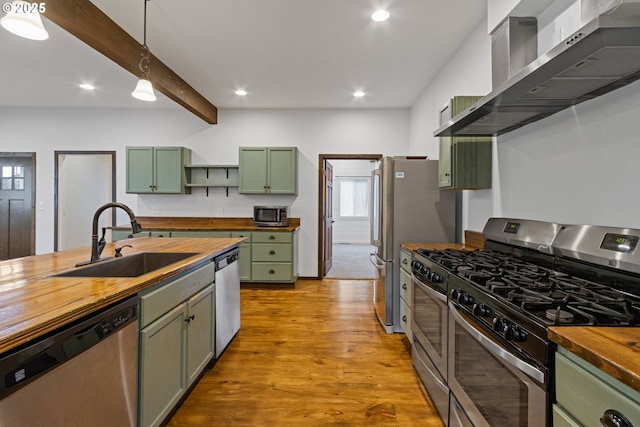 kitchen featuring stainless steel appliances, butcher block countertops, green cabinets, sink, and wall chimney range hood