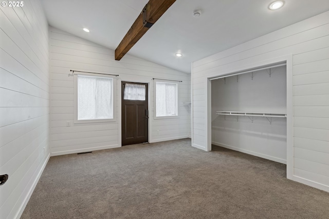 unfurnished bedroom with carpet floors, a closet, wooden walls, and vaulted ceiling with beams