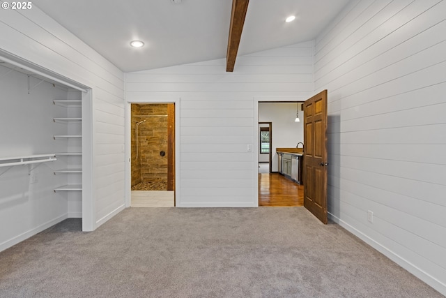 unfurnished bedroom featuring sink, light carpet, and vaulted ceiling with beams