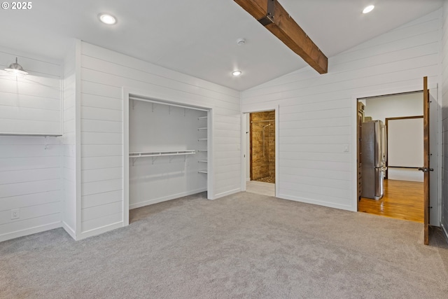 unfurnished bedroom featuring stainless steel fridge, lofted ceiling with beams, a closet, and carpet