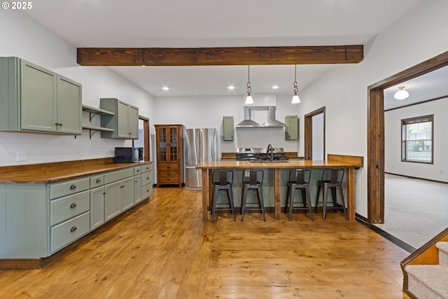 kitchen featuring green cabinetry, a kitchen bar, wooden counters, hanging light fixtures, and stainless steel fridge