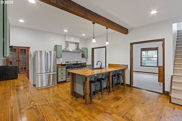 kitchen with sink, decorative light fixtures, wall chimney exhaust hood, wood counters, and appliances with stainless steel finishes