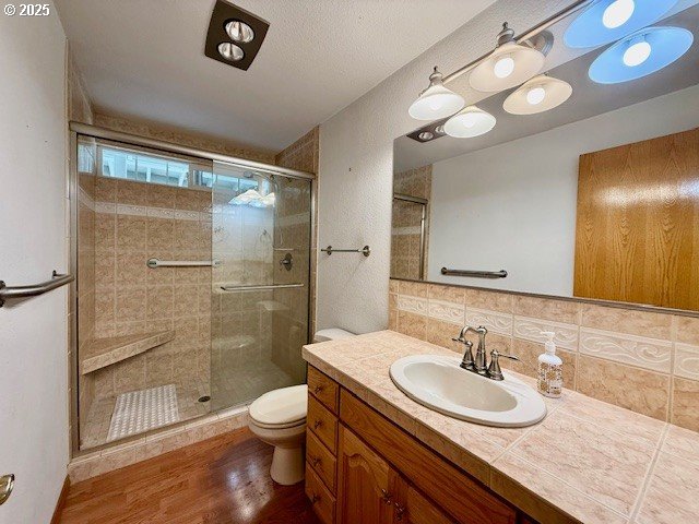 94504 Smokey Ln, Coquille, OR 97423 - full bath featuring toilet, a shower stall, vanity, wood finished floors, and decorative backsplash