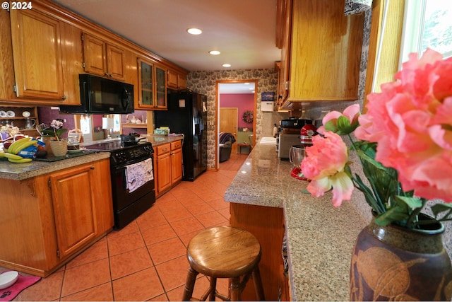 kitchen with a kitchen bar, light tile patterned floors, light stone countertops, and black appliances