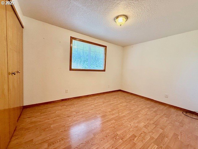 94504 Smokey Ln, Coquille, OR 97423 - unfurnished bedroom featuring a closet, light wood-style floors, baseboards, and a textured ceiling