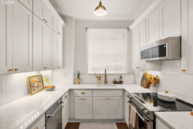 kitchen with appliances with stainless steel finishes, backsplash, sink, pendant lighting, and white cabinets