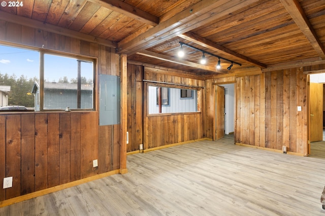 spare room featuring electric panel, track lighting, light hardwood / wood-style flooring, and wooden walls