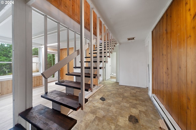 staircase featuring wood walls and a baseboard heating unit