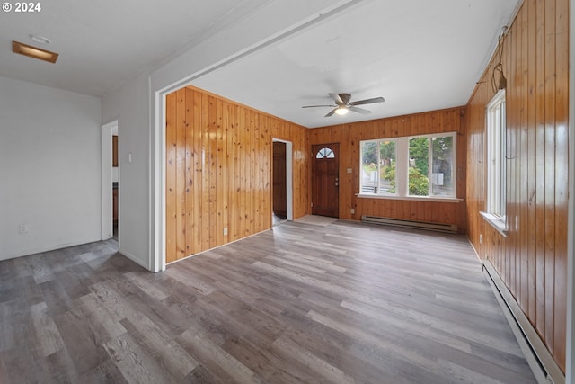 unfurnished room with baseboard heating, wood-type flooring, and wooden walls