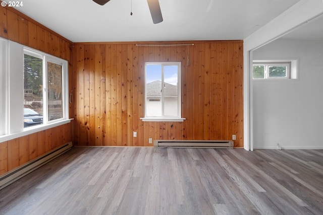 unfurnished room with wood walls, a baseboard heating unit, ceiling fan, and light hardwood / wood-style flooring