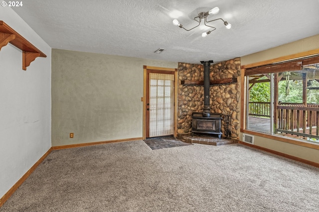 unfurnished living room featuring a wood stove, dark colored carpet, and a textured ceiling