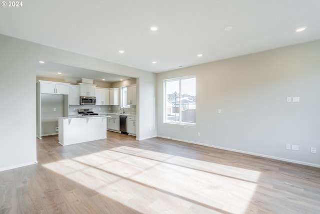 kitchen with appliances with stainless steel finishes, light wood-type flooring, a kitchen island, sink, and white cabinetry