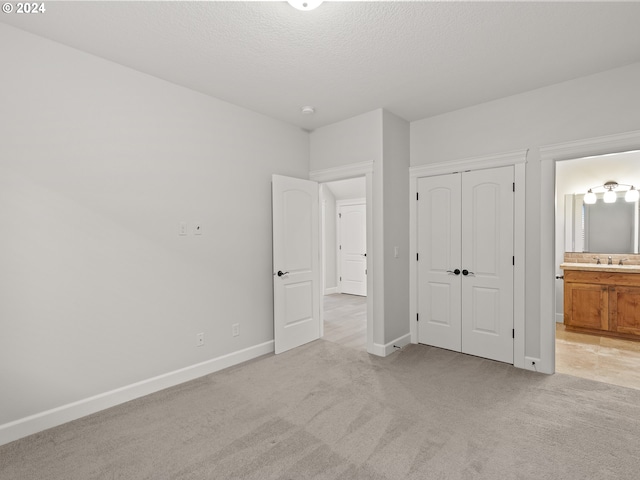 unfurnished bedroom featuring ensuite bathroom, a textured ceiling, light carpet, and sink