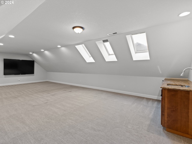 additional living space with light colored carpet, a textured ceiling, sink, and lofted ceiling