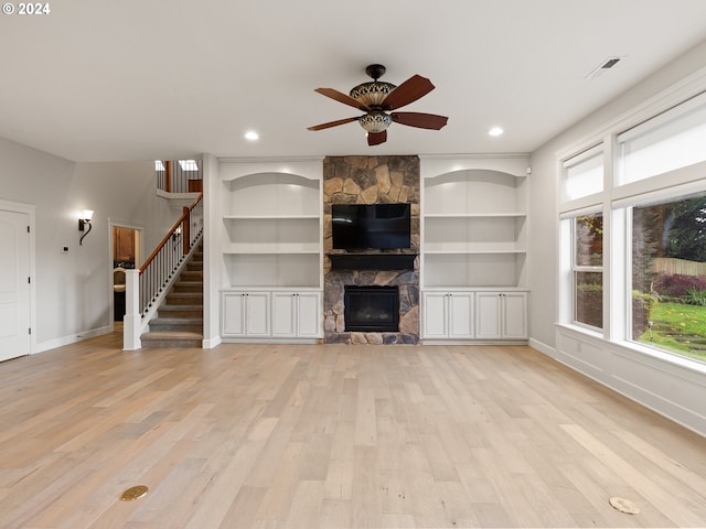 unfurnished living room featuring built in features, light wood-type flooring, ceiling fan, and a fireplace