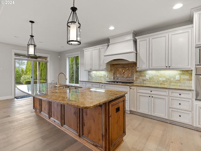 kitchen featuring sink, an island with sink, premium range hood, and white cabinets