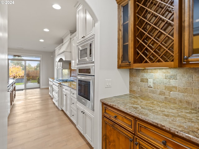 kitchen featuring light stone counters, stainless steel appliances, backsplash, light hardwood / wood-style floors, and white cabinets