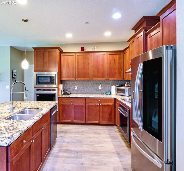 kitchen featuring light stone countertops, appliances with stainless steel finishes, sink, light wood-type flooring, and hanging light fixtures