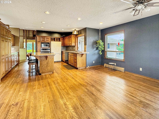 kitchen featuring a breakfast bar area, appliances with stainless steel finishes, a baseboard heating unit, and light hardwood / wood-style floors