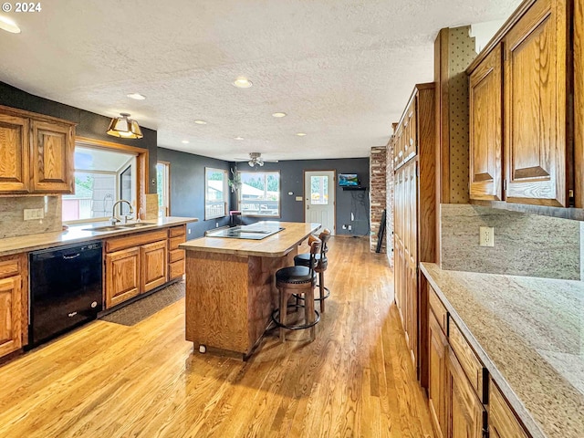 kitchen with sink, dishwasher, light wood-type flooring, a kitchen island, and a breakfast bar