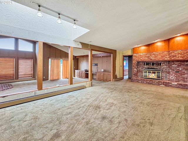 unfurnished living room featuring carpet, rail lighting, a textured ceiling, vaulted ceiling, and a fireplace