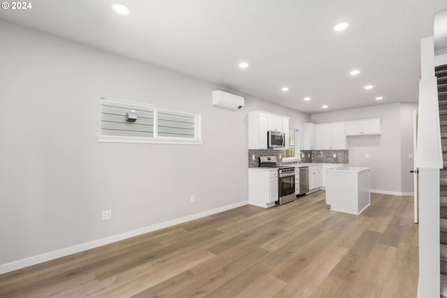 kitchen featuring appliances with stainless steel finishes, a wall mounted air conditioner, white cabinets, a kitchen island, and light hardwood / wood-style flooring