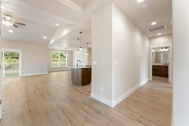 hallway with light wood-type flooring, a textured ceiling, and vaulted ceiling