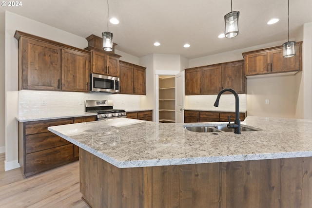 kitchen with appliances with stainless steel finishes, light hardwood / wood-style flooring, hanging light fixtures, and sink