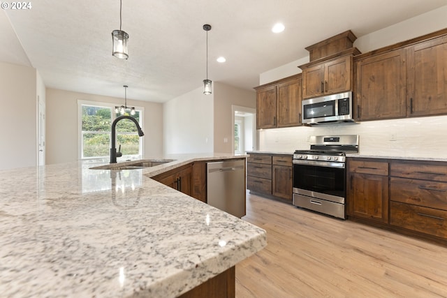 kitchen with decorative backsplash, stainless steel appliances, sink, pendant lighting, and light hardwood / wood-style flooring