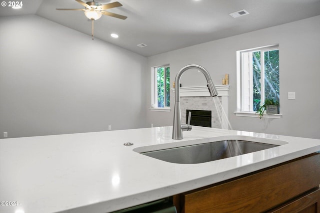 kitchen featuring visible vents, a sink, a fireplace, light stone countertops, and vaulted ceiling