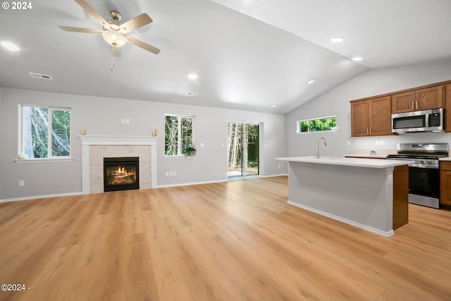 kitchen with light wood-type flooring, a tiled fireplace, appliances with stainless steel finishes, and a kitchen island with sink