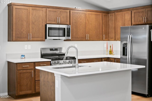 kitchen featuring vaulted ceiling, an island with sink, sink, appliances with stainless steel finishes, and light hardwood / wood-style floors