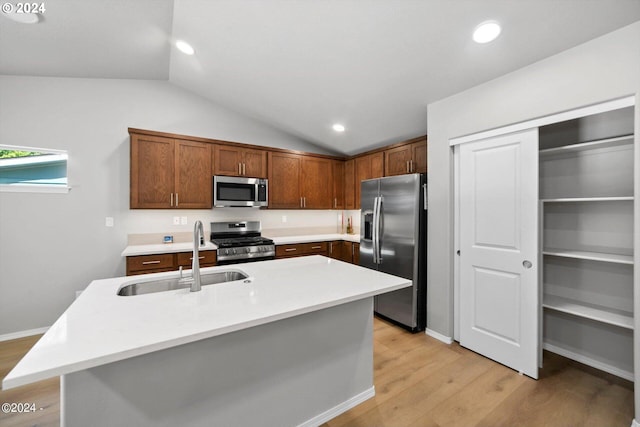 kitchen with an island with sink, stainless steel appliances, sink, lofted ceiling, and light wood-type flooring