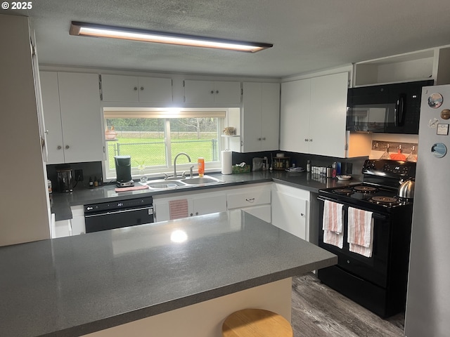 kitchen with sink, black appliances, kitchen peninsula, hardwood / wood-style flooring, and white cabinets