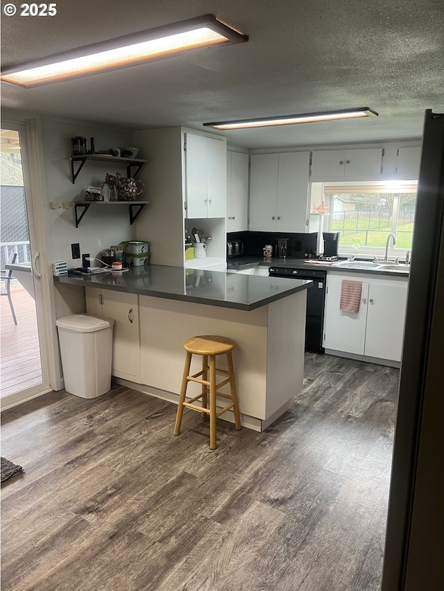 kitchen featuring a breakfast bar area, white cabinetry, dark hardwood / wood-style flooring, black dishwasher, and kitchen peninsula